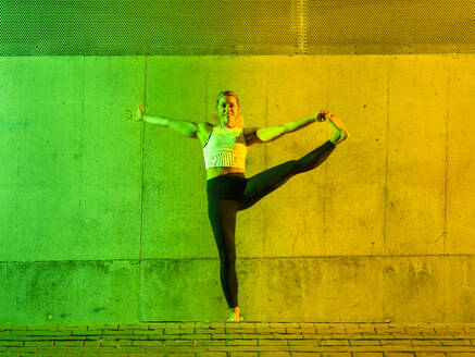 Happy woman doing yoga in front of neon colored wall - STSF03769