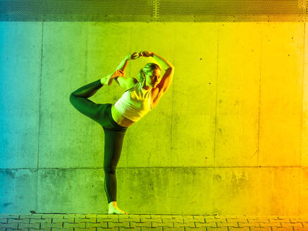 Woman doing yoga wearing sportswear in front of neon colored wall - STSF03770