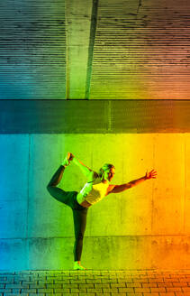 Woman doing bow pose yoga in front of neon colored wall - STSF03771