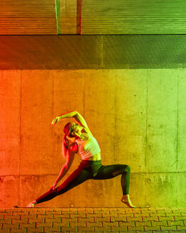 Aktive Frau beim Yoga in der Nähe einer neonfarbenen Wand - STSF03774