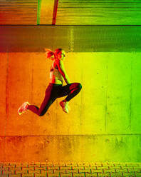 Active woman jumping in front of neon colored wall - STSF03776