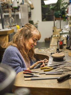 Lächelnder Goldschmied mit Arbeitswerkzeug in der Werkstatt - LAF02817
