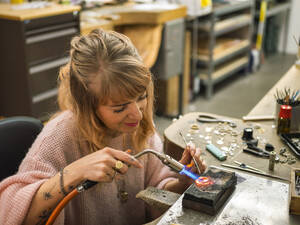 Smiling craftsperson welding gold ring at workshop - LAF02820