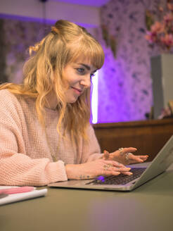 Happy freelancer wearing sweater using laptop at home - LAF02826