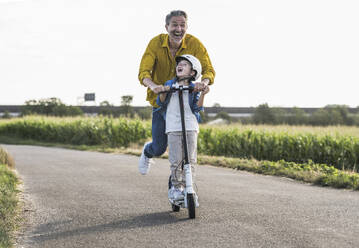 Fröhlicher Großvater genießt es, mit seinem Enkel auf der Straße Motorroller zu fahren - UUF30048