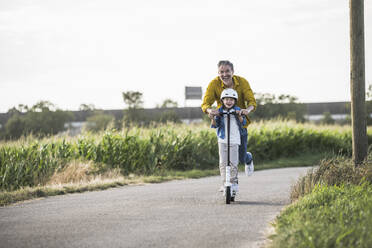 Ein glücklicher Mann genießt es, mit seinem Enkel auf der Straße einen Motorroller zu fahren - UUF30049