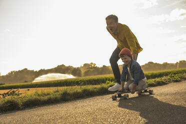 Boy enjoying skateboarding by grandfather on street at weekend - UUF30054