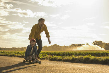 Happy boy enjoying skateboarding by grandfather on sunny day - UUF30055