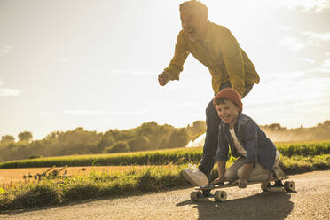 Fröhlicher Enkel hat Spaß und fährt mit dem Großvater Skateboard - UUF30056