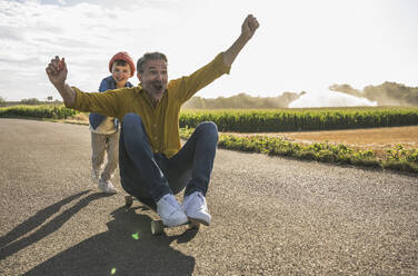 Fröhlicher Mann wird von Enkel auf Skateboard geschoben - UUF30063