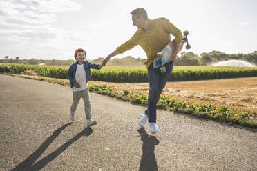 Cheerful boy holding hand of grandfather and running on road - UUF30065