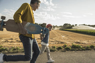 Happy grandson and grandfather running on street at sunny day - UUF30067