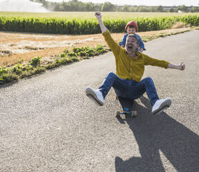 Glücklicher Mann beim Skateboardfahren und Enkel, der ihn von hinten schiebt - UUF30069