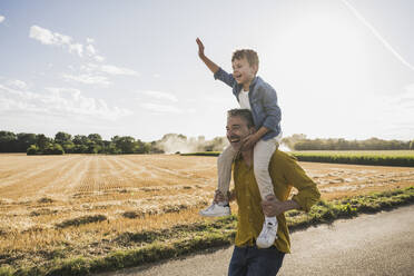 Man enjoying carrying grandson on shoulders at sunny day - UUF30074