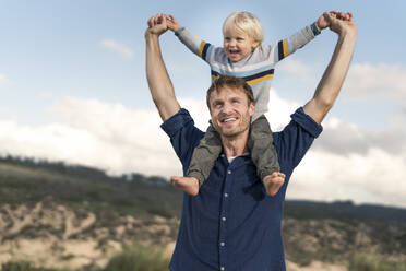 Lächelnder Vater trägt seinen Sohn auf den Schultern am Strand - SBOF03999