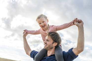 Happy man carrying daughter under cloudy sky - SBOF04011