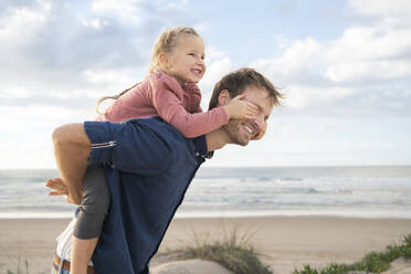 Happy father giving piggyback ride to daughter at beach - SBOF04023