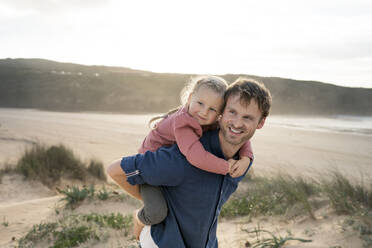 Lächelnder Vater, der seine Tochter am Strand huckepack nimmt - SBOF04025