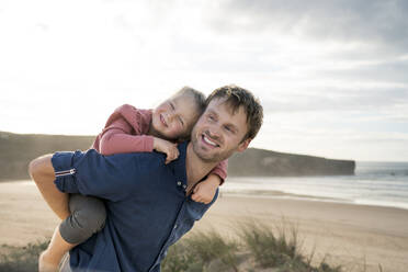 Happy father giving piggyback ride to daughter under sky - SBOF04027