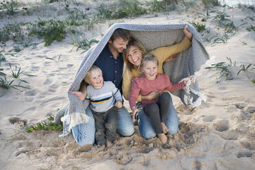 Glückliche Familie unter einer Decke im Sand am Strand - SBOF04029