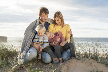 Glückliche Familie mit Decke am Strand sitzend - SBOF04030