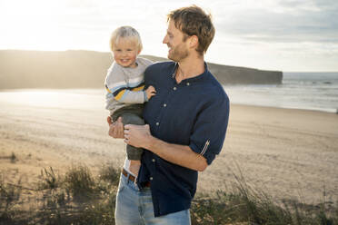 Happy father carrying son at beach - SBOF04037