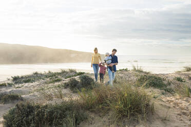 Happy family walking in front of sea at beach - SBOF04040