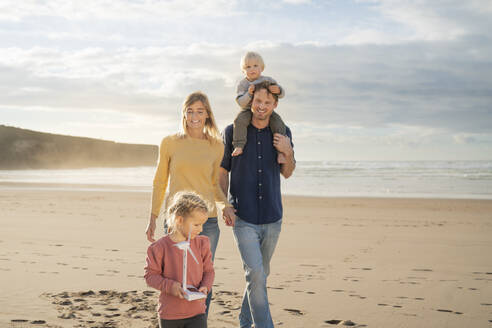 Lächelnder Vater und lächelnde Mutter mit Kindern am Strand an einem sonnigen Tag - SBOF04043