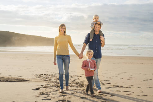 Glückliche Eltern, die sich an den Händen halten und mit ihren Kindern am Strand spazieren gehen - SBOF04044