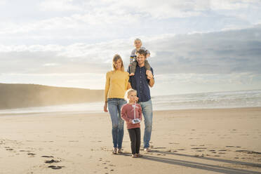 Happy father and mother walking with children on sunny day in front of sea - SBOF04045