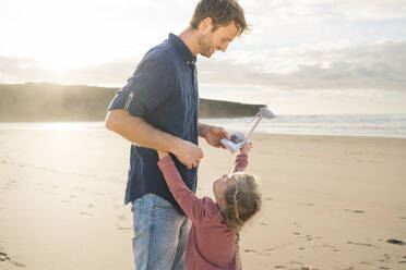 Glücklicher Vater mit Tochter, die an einem sonnigen Tag am Strand ein Windradmodell hält - SBOF04046