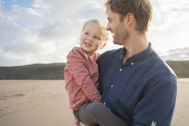 Smiling father and daughter at beach under cloudy sky - SBOF04050