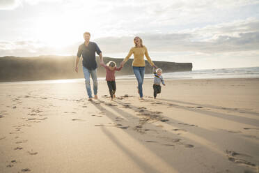 Glückliche Familie, die sich an den Händen hält und am Strand spazieren geht - SBOF04052