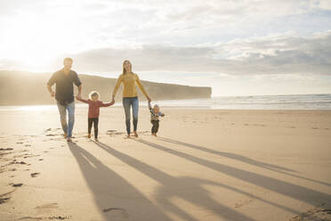 Happy family holding hands and walking at beach on sunny day - SBOF04054