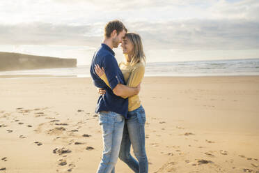 Glücklicher Mann und Frau umarmen sich vor dem Meer am Strand - SBOF04064