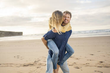 Happy man giving piggyback ride to woman at beach - SBOF04069