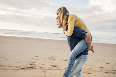 Smiling man giving piggyback ride to woman at beach - SBOF04070