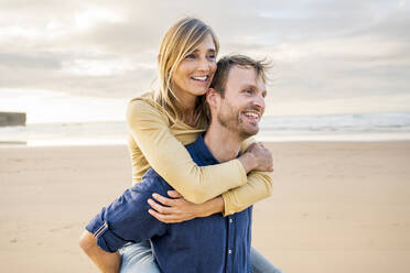 Happy man giving piggyback ride to woman at beach - SBOF04071