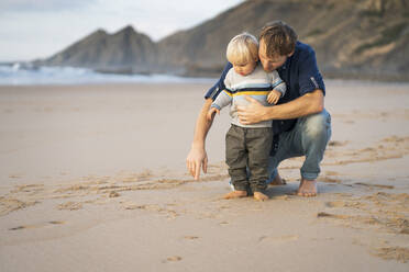 Boy with father pointing towards sand at beach - SBOF04077