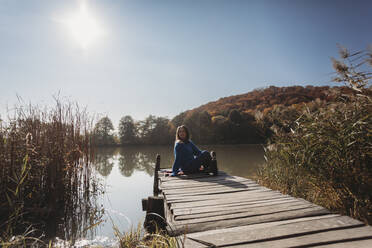 Woman looking at view sitting on jetty near lake - OSF02084