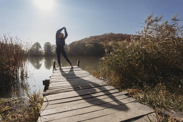 Woman standing with arms raised on jetty near lake - OSF02088