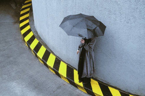 Woman holding umbrella standing near wall - YHF00093