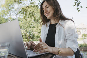 Lächelnde Geschäftsfrau mit Laptop am Tisch im Garten - OSF02094