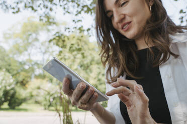 Lächelnde Geschäftsfrau mit Smartphone im Garten - OSF02096