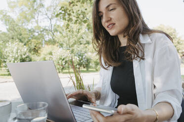 Lächelnde Geschäftsfrau arbeitet am Laptop am Tisch im Garten - OSF02097