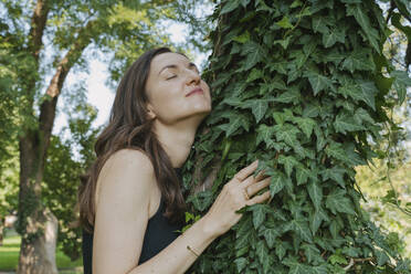 Smiling woman hugging tree in garden - OSF02101