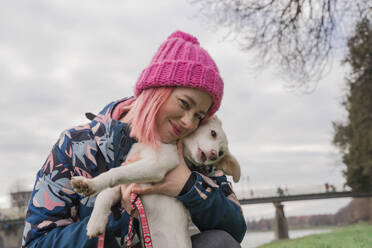 Glückliche Frau mit Strickmütze umarmt Hund im Garten - OSF02108