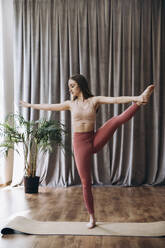 Young woman balancing on exercise mat at yoga studio - KANF00001