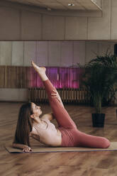Young woman stretching leg on mat in yoga studio - KANF00027