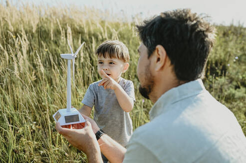 Vater und Sohn halten das Modell einer Windkraftanlage in einem Feld - ANAF02067